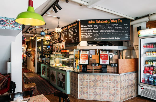 Counter at kebab shop with colourful lights hanging from ceiling and menu full of Turkish dishes