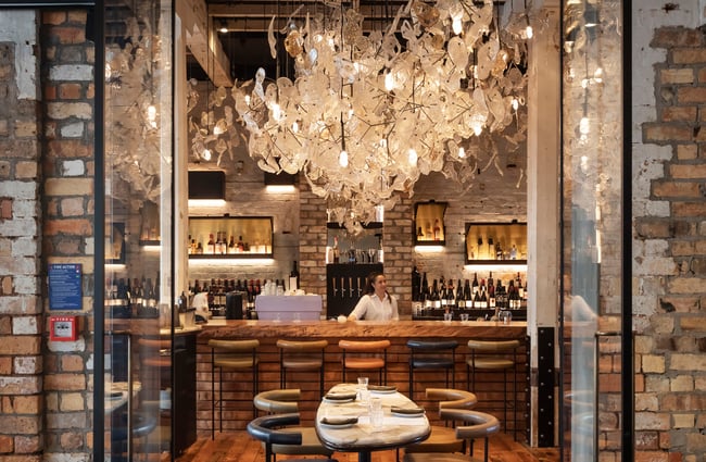 A staff member working behind at the bar inside a lush restaurant.