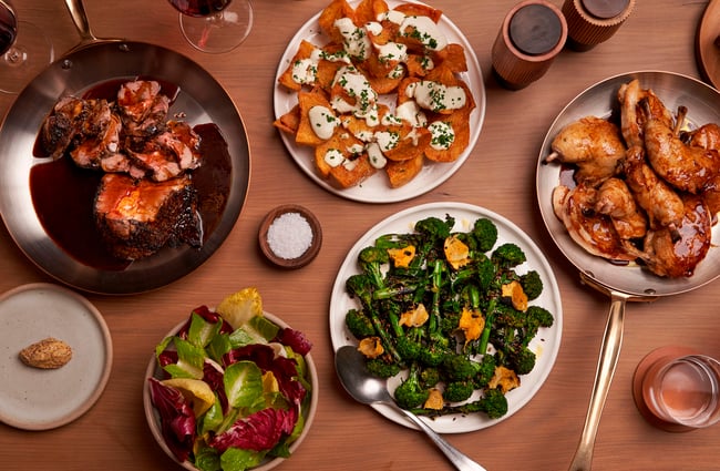 A flatlay of plates of meat and vegetables on a table.