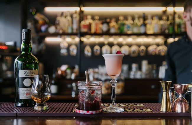 Whiskey glass, jar of jam and cocktail on the bar top.