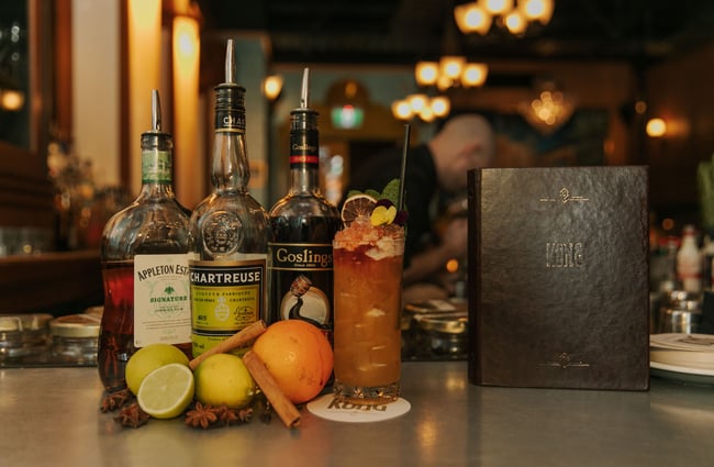 Cocktail with floral garnishes next to bottles of liquor on bar table