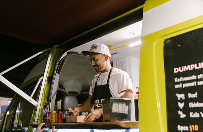 Alok smiling handing over box of dumplings from his food truck.