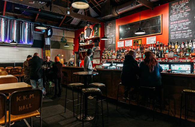 People sitting on high stools inside the red and black Last Place Bar in Hamilton.