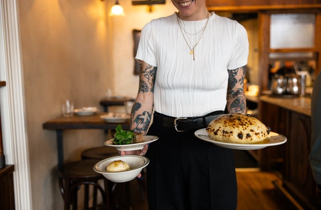 A woman smiling and holding three plates of food.