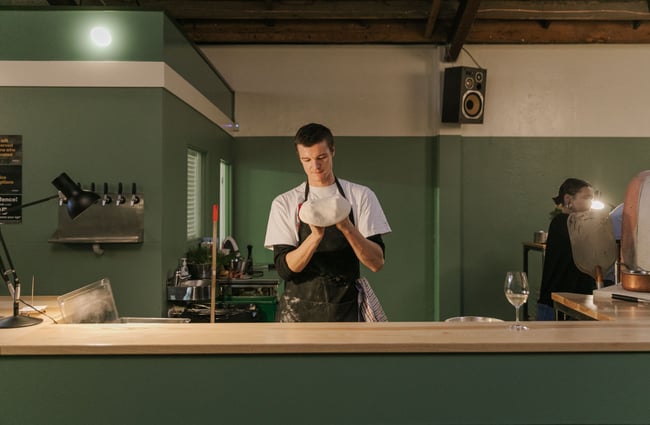 A chef making pizza dough behind a bar counter.