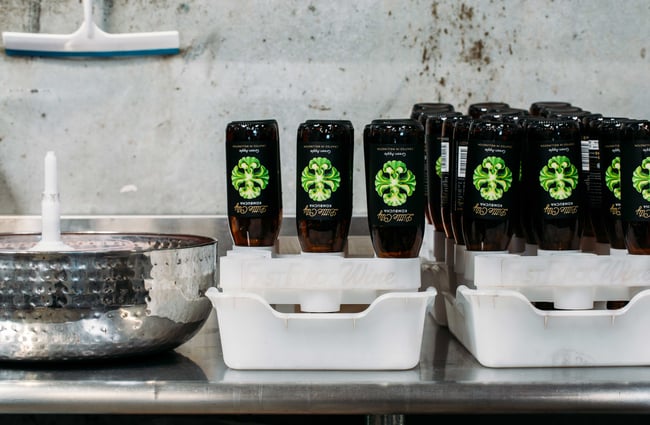 Dark brown glass bottles with green Little City Kombucha upside down in white buckets.