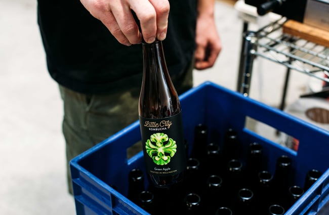 A kombucha brewery worker putting a bottle into a crate.