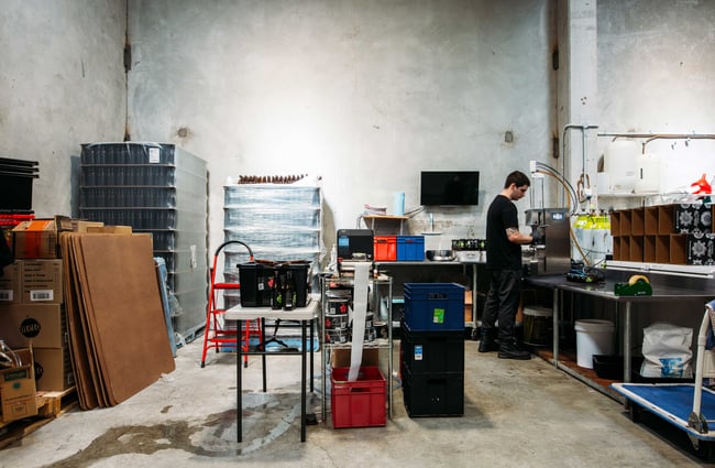 Inside the kombucha brewery workshop where there is a man working in a black top.