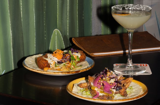 Two plates of tacos and a cocktail.