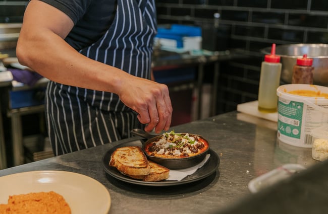 Close up of a chef's hand putting final garnishes on a meal in the kitchen at Little Pom's café, Christchurch.