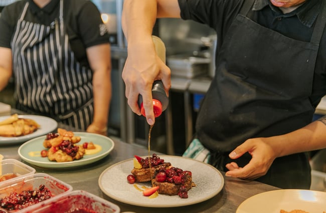 Close up of a chef drizzling syrup over a sweet meal in the kitchen at Little Pom's café, Christchurch.