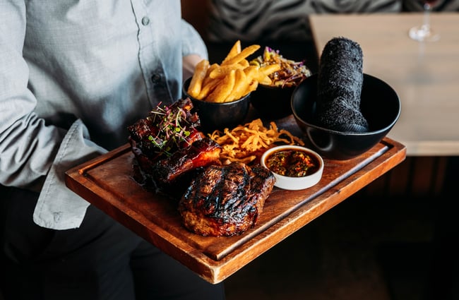 A staff member is holding a platter of meats and fries at Little Savanna.