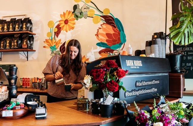 Barista pouring a coffee behind the machine at Love Stomp.