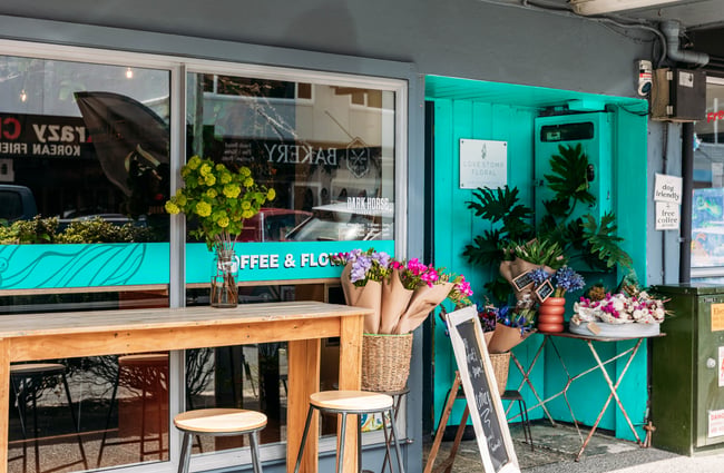 Turquoise exterior of a flower and coffee shop with bouquets of flowers on display outside Love Stomp.