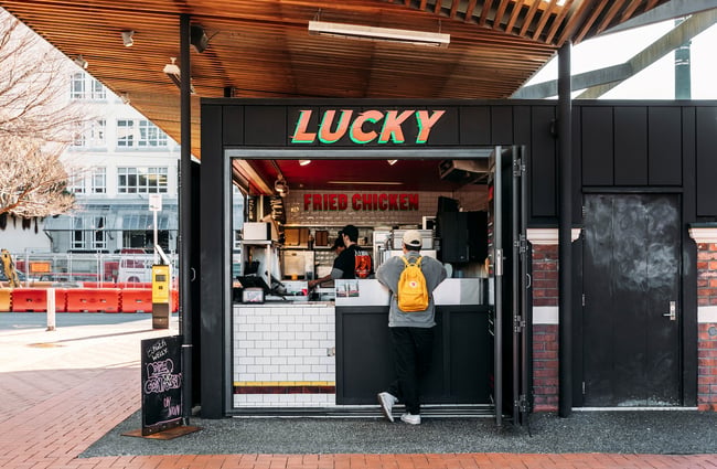 A person wearing a yellow backpack waits at the counter at LUCKY on Courtenay Place.