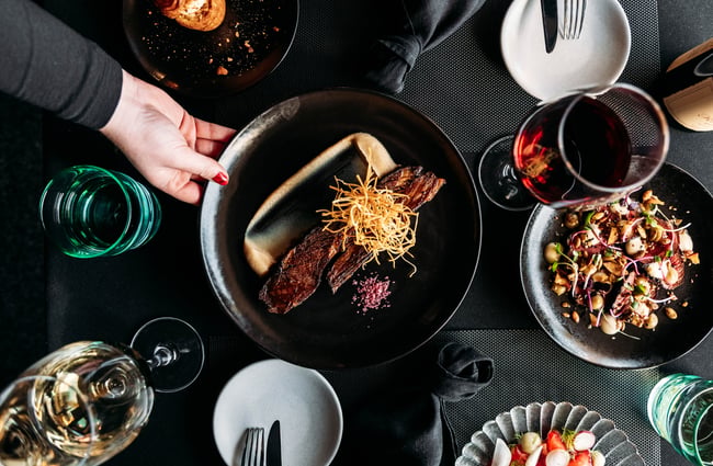 Staff member places a food dish down on the table with wine glasses and other plates.