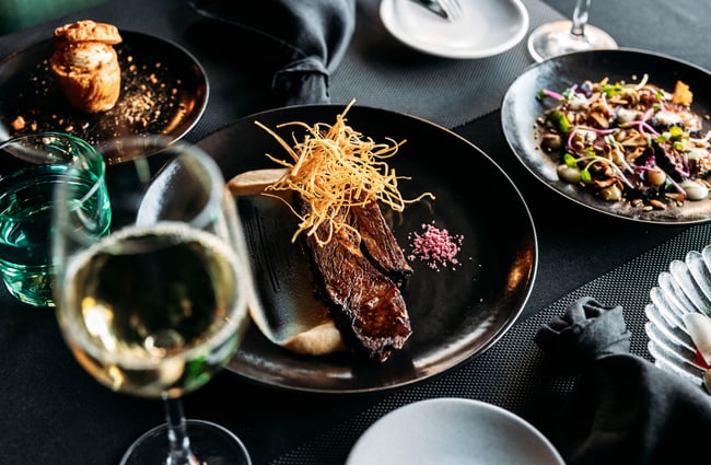 A main meal is on the table with a glass of wine in the foreground at Lustre.