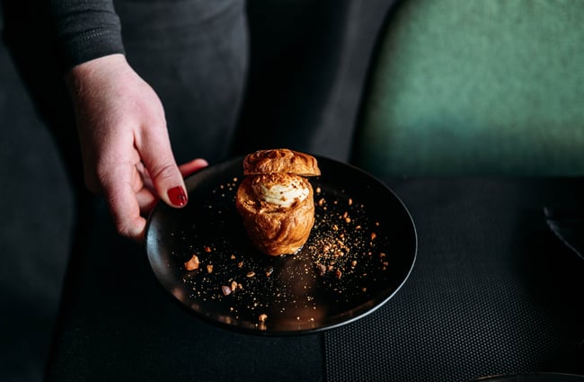 A staff member is serving a plate of dessert, placing it on the table at Lustre.