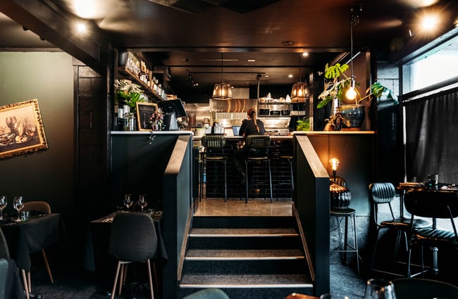 Tables and chairs are on a lower level dining area, with stairs leading up to a bar area at Lustre.