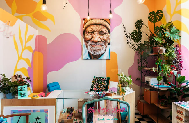 Colourful art shop with a vibrant yellow and purple mural, portrait of an old man, plants and jewellery