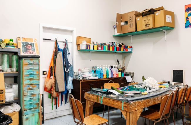 Art workshop room at Luzette with shelves of paint and paintbrushes and a desk with artworks in progress