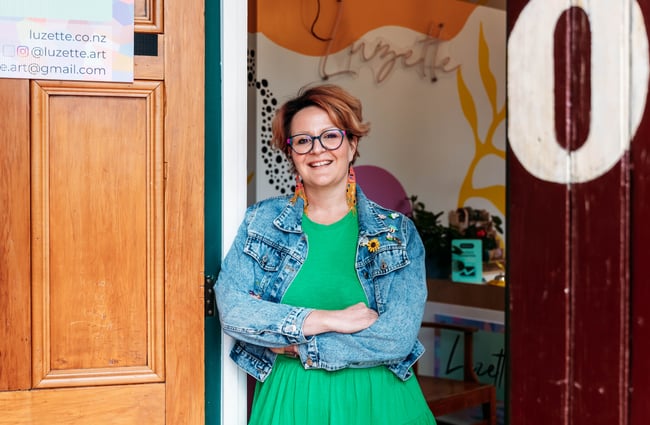 Luzette standing smiling outside her art shop and studio in Ōamaru