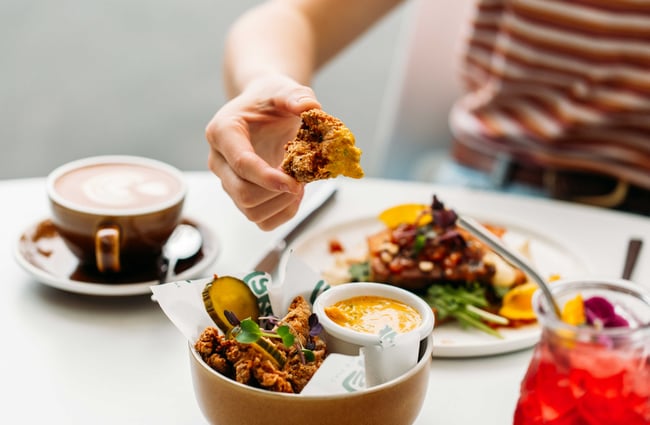 A hand holding fried chicken at a white table.