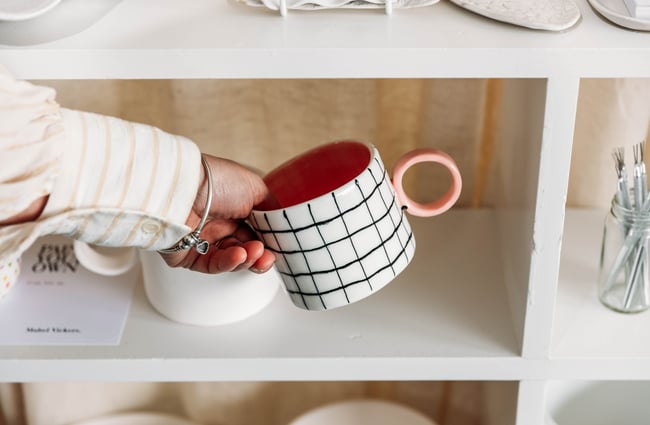 Customer selecting a checked mug with a pink handle from the shelf at Mabel Vickers.