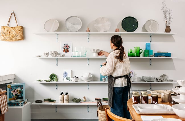 Shop assistant is placing a ceramic piece on one of the shelves on the wall at Mabel Vickers.