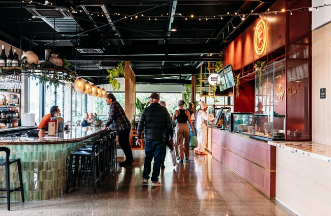 A customer standing at a bar area to order, while other customers walk by.