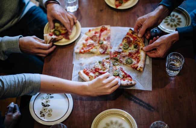 Hands reaching for slices of a pizza in the middle of the table at Mamma Mia.