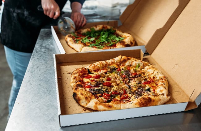 Pizza in takeaway boxes being sliced up at Manakau Market.