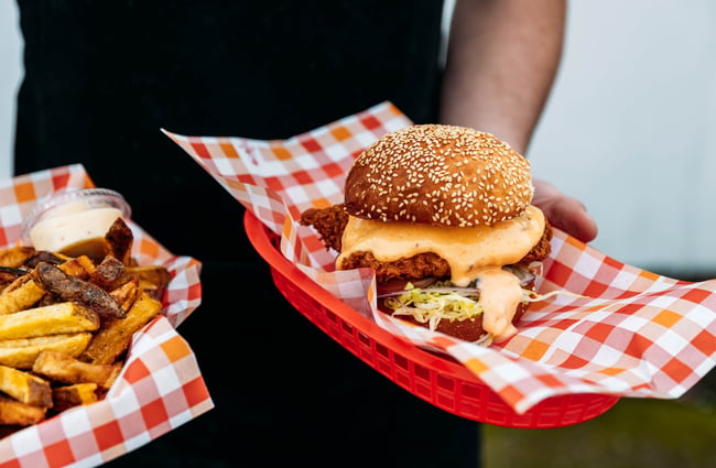 Shop assistant holding a plate of smashburgers and fries at Manakau Market.