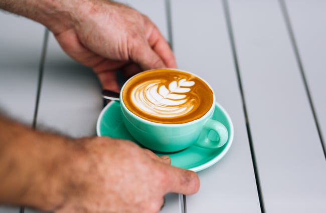 Man puts coffee on table at Manuka Brothers, Hamilton.