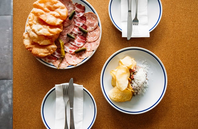 A flat of slices of meat and crisps on a table.