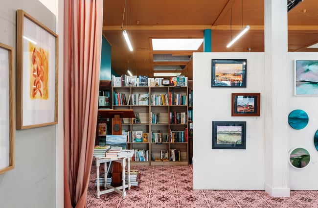 Artwork displays on the wall and bookshelves behind them at Mewington's Book Shoppe.