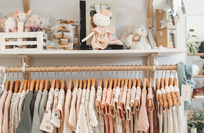 Baby clothing on wooden hangers and baby toys on the shelf above.
