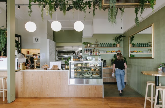 A staff member walking behind the counter inside the bright and colourful cafe space at Mint Folk and Co in Twizel.