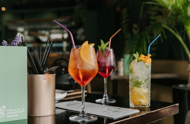Three different cocktails on a black table with straws.