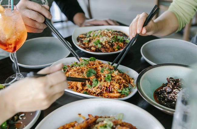 Crowd of people eating a plate of noodles with chopsticks around a table at Miss Peppercorn.
