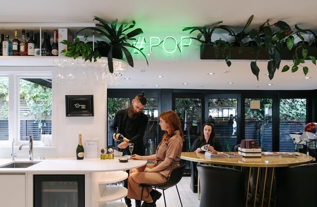 Woman being poured a glass of bubbles at Mod's Hair, Christchurch.