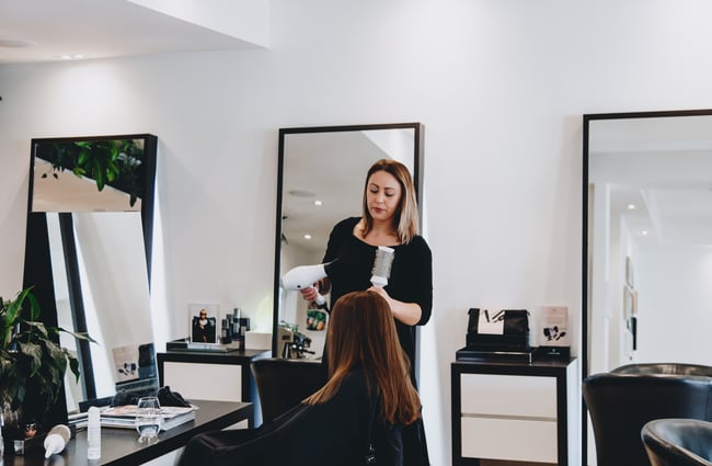 A woman blow drying hair inside Mod's Merivale hairdresser in Christchurch.
