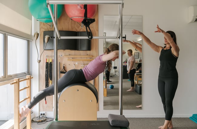 A pilates teacher assisting a client on a pilates machine.