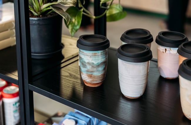 Reusable coffee cups on a shelf.