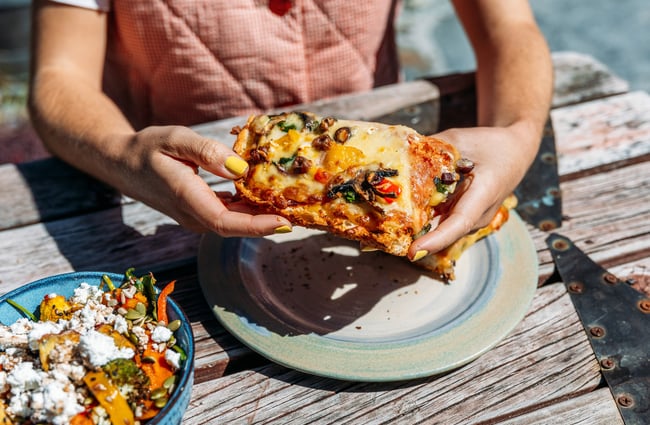 Hands holding a large piece of pizza bread.