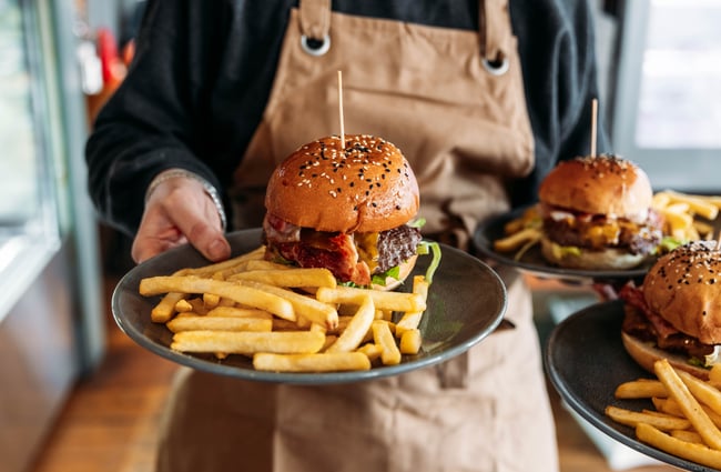 Hands holding plates of burgers and fries.