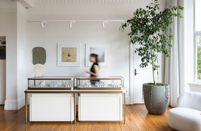 Wide shot of jewellery showroom with cabinet full of jewellery and a shop assistant behind at Naveya & Sloane Jewellery.