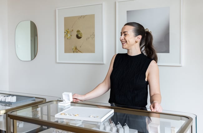 Shop assistant stands behind jewellery cabinet and is smiling at Naveya & Sloane Jewellery.