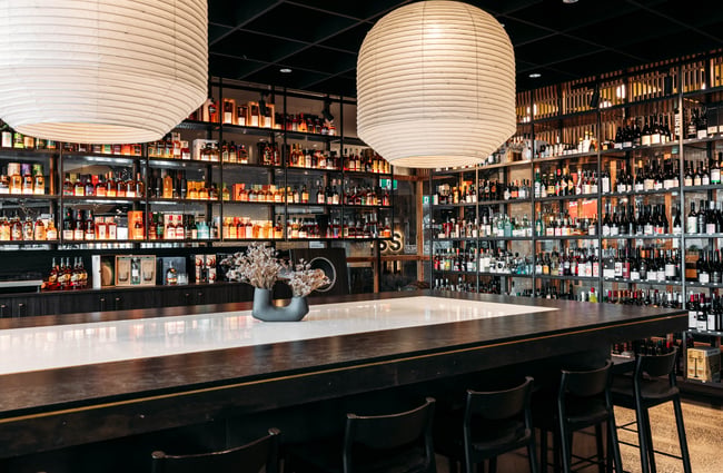 Bar in the middle of the room and shelves of alcohol behind at Neat at Made.