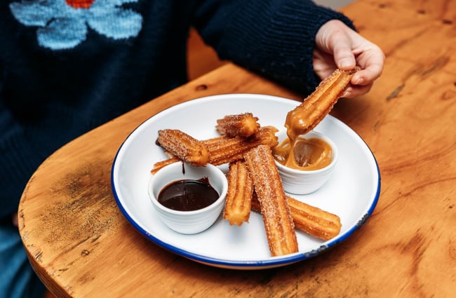 Churros being dipped into caramel sauce.